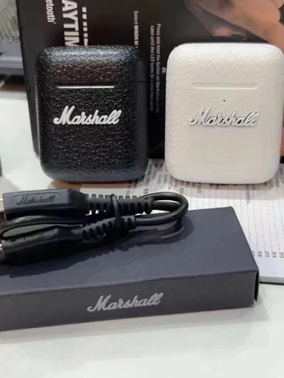 Black and cream compact speakers with a charging cable and packaging