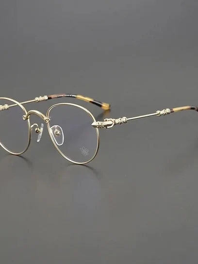 A pair of thin gold round-frame glasses photographed against a plain grey surface