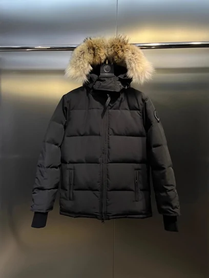 A black hooded parka with a thick fur trim, photographed hanging against a pale wall