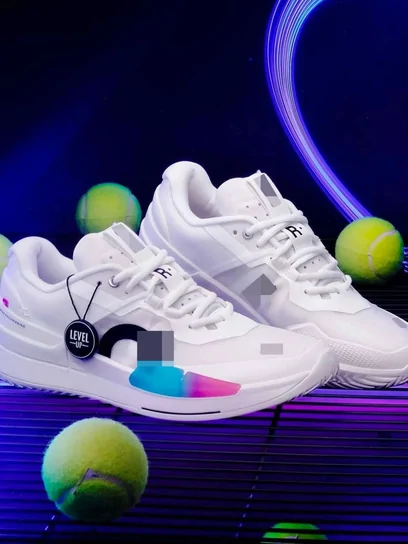 A white running shoe lit against a dark blue backdrop with tennis balls scattered behind it