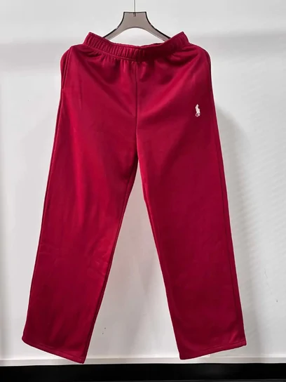 A pair of deep red sweatpants on a wooden hanger against a pale wall
